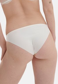 Witte katoenen slipjes met een gladde textuur en minimale bedekking, met een eenvoudig ontwerp en een elastische tailleband van lichte kwaliteit.