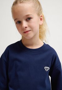 Mörkblå bomullströja med rund halsringning, med en liten broderad logotyp på bröstet och löst sittande ärmar.