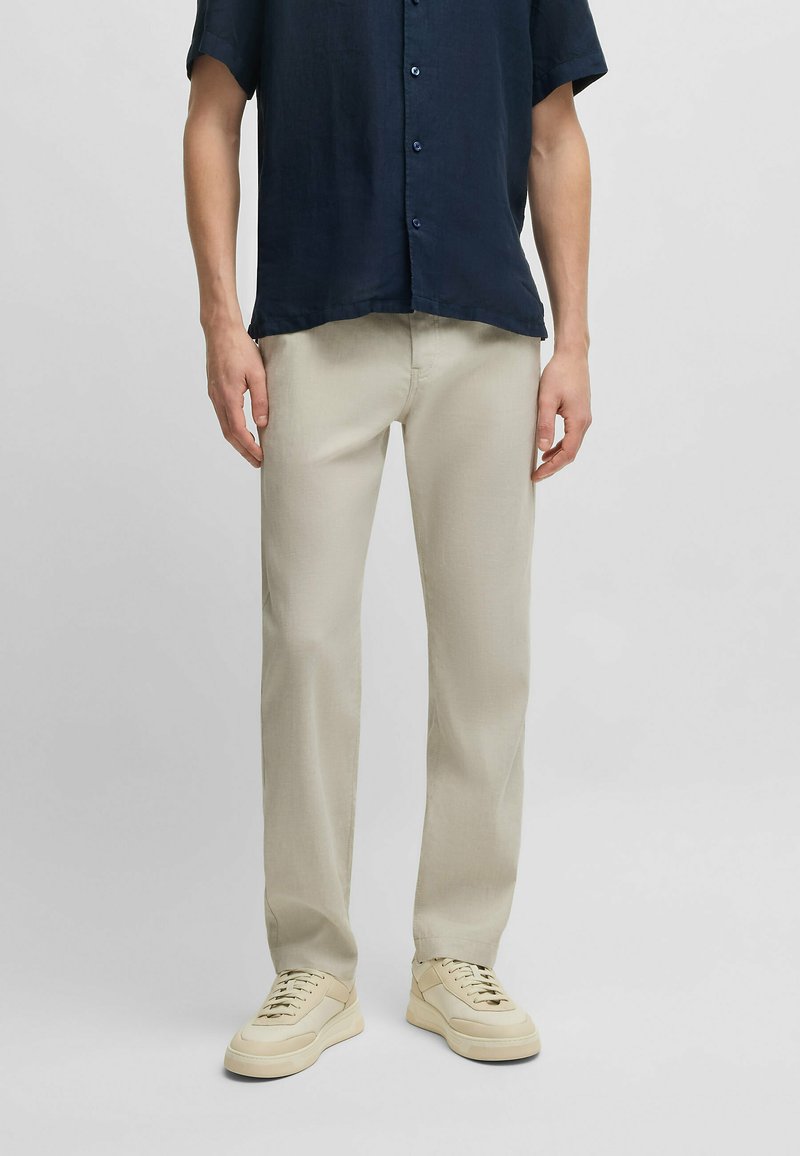 Beige trousers made of lightweight fabric with a straight cut, paired with a dark navy short-sleeve shirt and light sneakers.