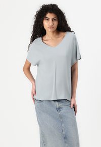 Lys grå V-hals t-shirt med korte ærmer, lavet af et glat materiale. Kombinationen med en højtaljet denimskirt, der har en søm foran.