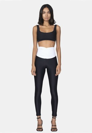 Black crop top with wide straps, high-waisted black leggings featuring a white, gathered waistband, completed with black strappy heels.
