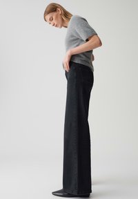 Maglione corto a maniche corte grigio chiaro in maglia pelosa abbinato a jeans scuri a vita alta e a gamba larga. Stivali neri a punta visibili.