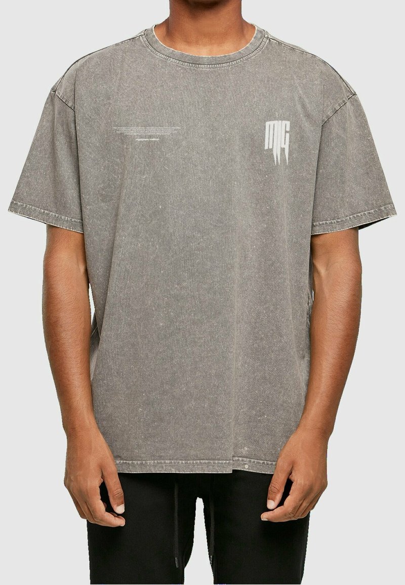 Grå oversized bomulds T-shirt med korte ærmer, rund hals og diskrete grafiske detaljer på brystet. Teksturfinish og slidseret udseende.