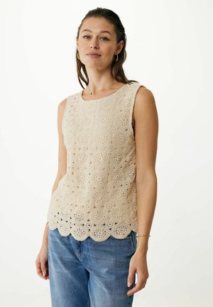 Beige crochet tank top with floral patterns, rounded neckline, and scalloped hem. Worn with light blue, loose-fitting jeans.