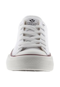 Vita canvas sneaker med gummisula, detaljerad sömnad och en marsalakkss accent runt sulan. Har platta snörningar och en logotyp på plosen.