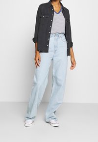 Černá denimová košile s knoflíkovým zapínáním, pruhované tričko s v-výstřihem, světle modré volné džíny a bílé tenisky. Pohodlný vrstvený outfit.