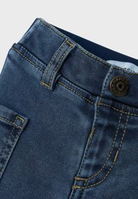 Jeans in denim blu caratterizzati da un tessuto testurizzato, cuciture gialle a contrasto, chiusura con bottone e tasche laterali.