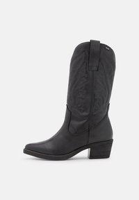 Bota de cowboy de cuero negro con punta afilada, costuras decorativas y tacón bajo de altura media. Asa trasera para ponerla con facilidad.