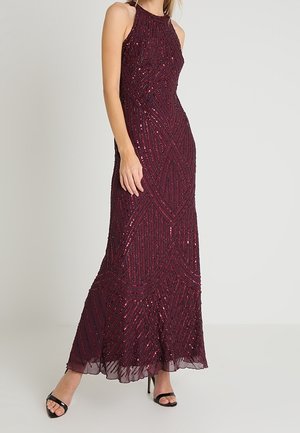 Abito da sera bordeaux senza maniche con motivi geometrici di paillettes, corpetto aderente, orlo svasato, indossato con tacchi neri aperti.