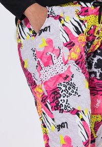 Bunte Hose mit einer Mischung aus Tiermustern in Pink, Gelb und Schwarz, mit einer weichen Textur und seitlichen Taschen.