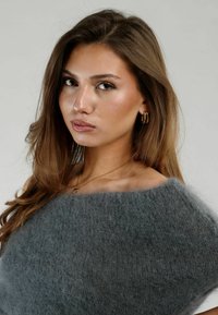 Suéter gris, fuzzy y de gran tamaño con un escote amplio, que presenta una textura suave y un ajuste holgado. Pendientes de aro dorados y un delicado collar dorado.