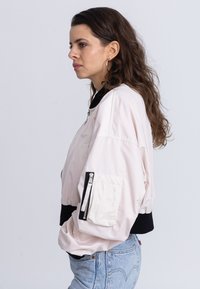 Helles rosafarbene Bomberjacke mit schwarzem geripptem Saum und Kragen. Verfügt über eine mit Reißverschluss gesicherte Taschen am Ärmel und hat eine weiche, glatte Textur. Lässiger Schnitt.