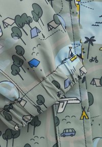 Lekki materiał w przygaszonej zieleni z fantazyjnymi wzorami drzew, namiotów, samochodów i samolotu; zawiera detal z elastycznym mankietem.