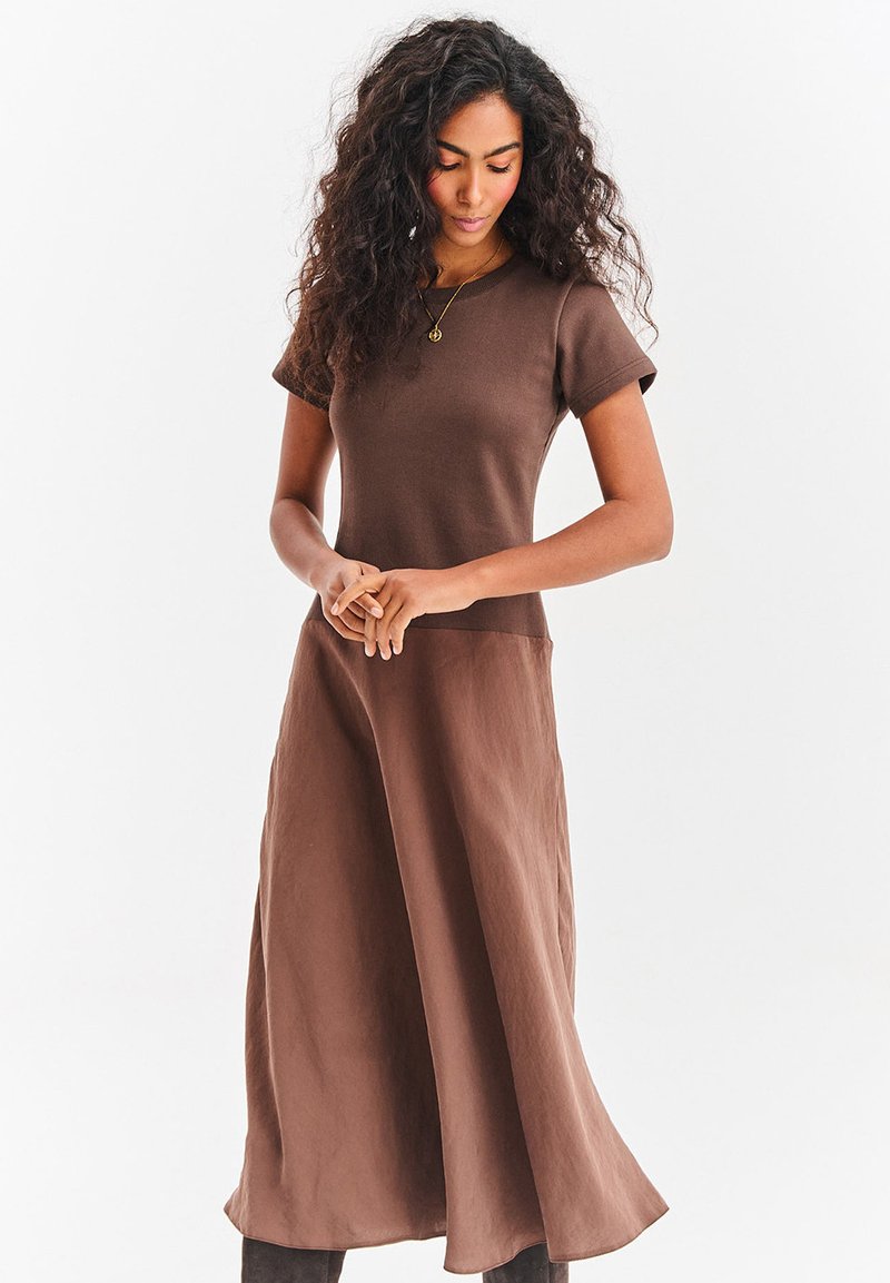 Brązowa sukienka wykonana z miękkiej tkaniny, z okrągłym dekoltem, krótkimi rękawami i luźną sylwetką sięgającą do połowy łydki.