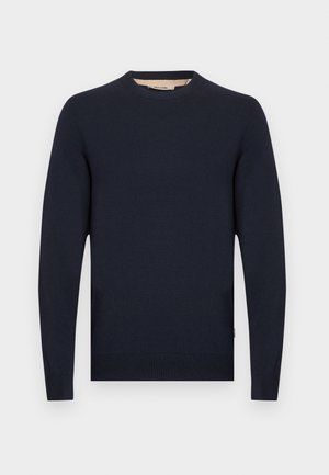 Tengerészkék pulóver kerek nyakkal, hosszú ujjakkal, és bordázott mandzsettákkal és derékpánttal. Simább anyagból készült, laza, kényelmes szabással.