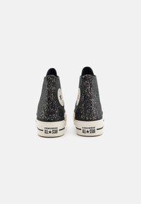Zwarte high-top sneakers met een gespikkelde textuur, witte rubberen zolen en het Converse-logo aan de zijkanten. Voorzien van een gewatteerde kraag.