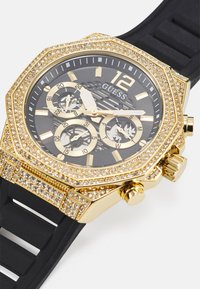Orologio ottagonale in tono oro con quadrante nero, dettagli in cristallo, tre sotto-quadranti e cinturino in gomma nera. Caratterizzato da indicatori delle ore audaci e logo.