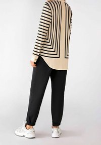 Černý a krémový top s dlouhým rukávem s výrazným pruhovaným vzorem, doplněný volnými černými kalhotami a světle zbarvenými sportovními botami.