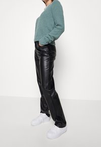 Pantalones de piel sintética negros con costuras laterales y bolsillos, combinados con un suave suéter de lana difusa en tono verde azulado. Zapatillas blancas completan el conjunto.