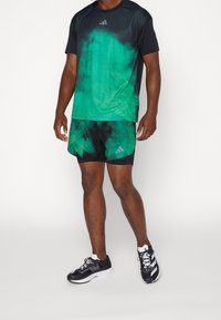 Grön och svart batikmönstrad atletisk t-shirt och matchande shorts i lättviktig tyg; har Adidas-logotyp på båda plaggen.