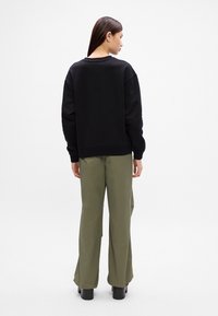 Čierna mikina s obľúbeným výstrihom, vo voľnej veľkosti, a rebrovanými manžetami, skombinovaná s olivovozelenými širokými nohavicami a robustnou čiernou obuvou.