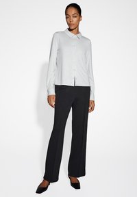 Camicia a maniche lunghe grigia chiara con colletto abbinata a pantaloni neri a gamba larga e scarpe slip-on nere. Tessuto liscio, vestibilità su misura.