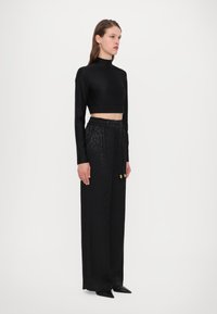 Zwarte cropped top met lange mouwen, gecombineerd met hooggetailleerde zwarte broeken met een subtiel luipaardpatroon en gouden knoopaccenten.
