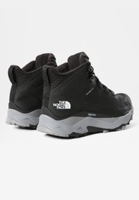 Černé turistické boty s texturovaným textilním svrškem, gumovou podrážkou a výrazným brandingem. Mají vysoký design kotníku a zesílenou špičku.