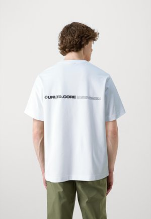 Kurzärmliges weißes Baumwoll-T-Shirt mit rundem Halsausschnitt und schwarzem Text-Logo auf dem Rücken, kombiniert mit olivgrünen Hosen.