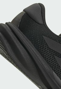 Scarpa da ginnastica nera con tomaia in tessuto texture, suola in gomma con motivi rigati e design elegante con accenti di branding discreti.