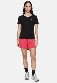 Zwarte t-shirt met korte mouwen en witte kraagdetails, gecombineerd met roze shorts, zwarte sokken en zilveren sportschoenen. Fila-logo op het shirt.