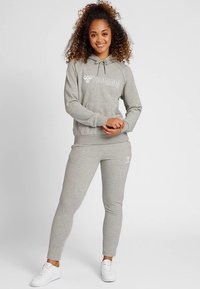 Szara bluza z kapturem i białym logo, zestawiona z dopasowanymi spodniami. Obie wykonane z miękkiej tkaniny, z prążkowanymi ściągaczami na mankietach i dole.