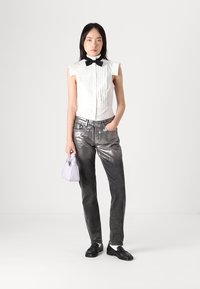 Top blanco con pliegues y un lazo negro, jeans metálicos plateados y un pequeño bolso lila. Zapatos negros completan el atuendo.