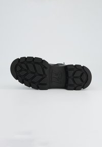 Suela de zapato de goma negra con un diseño de banda de rodadura intrincado y un logotipo, que presenta una base plana y un acabado texturizado para agarre.