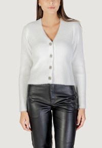 Cardigan bianco a maniche lunghe con scollo a V, finitura testurizzata e cinque bottoni decorativi. Abbinato a pantaloni in pelle neri aderenti.