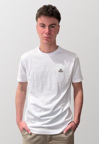 T-shirt in cotone bianco con un piccolo logo ricamato in blu e marrone. Design semplice con collo a giro e maniche corte. Tessuto morbido.