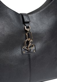 Černá texturovaná kožená kabelka se zlatým geometrickým a iniciálou "G" dekorativním kováním připevněným blízko horního středu.