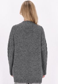 Cardigan gri tricotat cu un design texturat, umeri căzuți și mâneci lungi. Prezintă un guler cu nervuri și o croială relaxată.