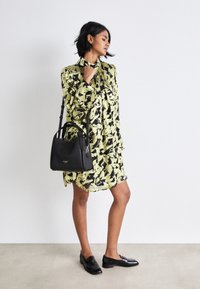 Svart og gul blomstret kjole med krage og flytende design. Svart veske med en strukturert form. Svart loafers fullfører antrekket.