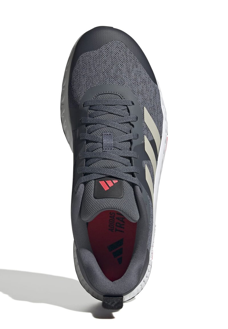 Zapatilla deportiva gris oscuro con un upper de malla texturizada, cordones elásticos y tres rayas blancas. El interior presenta una plantilla roja y un logotipo.