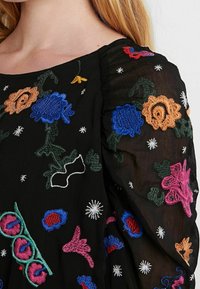 Schwarzer transparenter Stoff mit buntem Blumenstickerei in Blau, Pink, Orange und Grün. Verfügt über strukturierte Details und subtile Sternmuster.