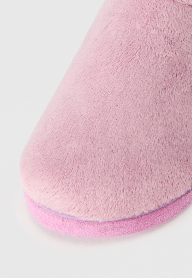Pantufla de felpa rosa con punta redondeada, textura suave y suela de un rosa claro. El material de la parte superior parece esponjoso y acogedor, diseñado para la comodidad.