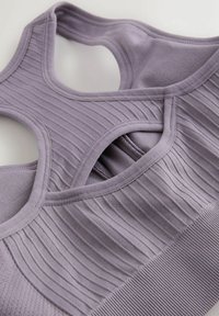 Gaiši lavandas tonī sporta krūšturis ar ribotu faktūru un parādskriemeļa dizainu. Audums ir gluds un elastīgs, ar bezšuvju apdari.
