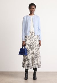Lichtblauwe cardigan, witte top, zwart-wit gestreepte rok, kniehoog zwarte laarzen en een kleine blauwe handtas. Geverfd breiwerk, knoopdetails.