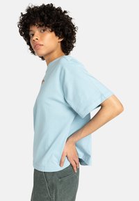T-shirt bleu clair à manches courtes avec un col rond, fabriqué en tissu doux, avec un petit graphique coloré à l'avant.