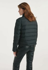 Czarna kurtka puchowa z poziomym wzorem przeszyć, wysoki kołnierz i krótszy krój. Noszona z czarnymi skórzanymi spodniami, podkreślająca elegancki styl.