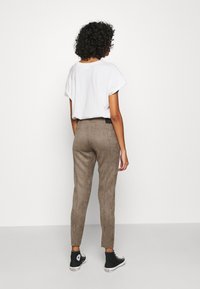 Pantalon en daim marron avec une coupe slim, associé à une chemise blanche unie et des baskets montantes noires, vu de dos.