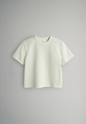 Trumparankovė marškinėliai su apvalia iškirpte, pagaminti iš tekstūruotos smėlio baltumo medžiagos. Paprastas dizainas, laisvas siluetas ir tiesi apačia. Be matomų raštų ar detalių.