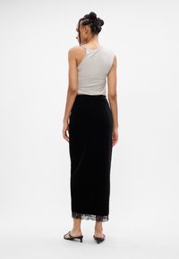 Szürke, rövidített tank top fekete, testhezálló velúr szoknyával, amely csipkés szegéllyel rendelkezik, fekete, nyitott orrú magassarkú szandállal párosítva.