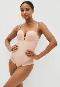 Bodysuit in huidskleur met een diepe v-hals, verstelbare banden en doorschijnende stippenaccenten aan de zijkanten, gemaakt van een soepele stof.